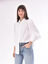 Camisa blanca a rayas verticales, de corte clásico, cuello camisero y mangas largas abullonadas con puños abotonados.