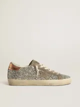 Zapatillas deportivas estilo urbano con upper completamente cubierto de glitter plateado. Presentan detalles en gamuza color arena, incluyendo la estrella lateral característica. El talón tiene un acabado metálico color cobre. La suela es de goma color beige con efecto desgastado.