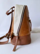 Mochila pequeña de cuero color camel, con base marrón, laterales color crema y cierre superior con cremallera.