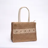Bolso de yute color marrón claro con diseño geométrico en blanco y doble asa de mano.