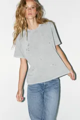 Camiseta gris de algodón con cuello redondo y manga corta. Tiene apliques de strass plateado en el frente.