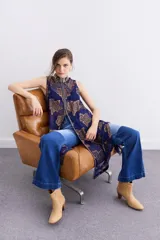 Camisa larga sin mangas confeccionada en viscosa azul con estampado de flores doradas y cuello mao. Presenta bordados en cuello y cartera frontal, y cierre frontal con cremallera.