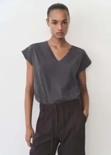 Camiseta gris con cuello en V, manga corta y detalle de tachuelas en los hombros.