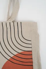 Bolso tote de tela con estampado de rayas verticales rosadas y blancas, laterales y asas en color beige. Presenta la palabra "BONJOUR" en verde en el centro y "INDIAN" en la parte inferior.