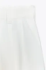 Pantalón blanco de tiro alto con pinzas delanteras, bolsillos laterales y cintura elástica en la parte trasera.