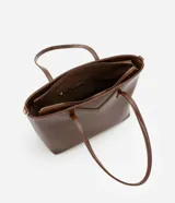 Bolso shopper grande color marrón de material sintético con doble asa, una fija y otra larga desmontable. Tiene cierre de cremallera y detalles de recortes.