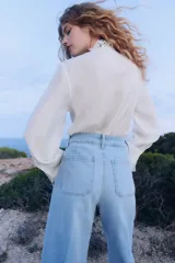 Blusa blanca de corte holgado en tejido transparente de mezcla de lyocell. Modelo de manga larga con cuello elevado de encaje, puños anchos abotonados y bajo recto. Pechera con abertura, alforzas y tiras spaghetti.