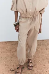 Pantalón de tiro medio color beige, con cintura elástica ajustable con cordones, bolsillos delanteros y puños elásticos en los tobillos.