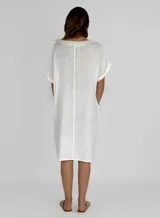 Vestido blanco de lino, corte recto, con cuello en V, mangas cortas con dobladillo y bolsillos laterales.