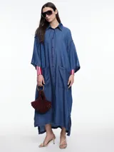 Vestido camisero largo de denim liviano de lyocell azul, de silueta relajada, mangas 3/4 amplias y hombro caído. Cuenta con bolsillos grandes aplicados en el frente, tajos laterales y botones a contratono.