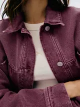 Chaqueta corta de denim color borgoña con cuello clásico, cierre frontal con botones metálicos y bolsillos de parche en el pecho.