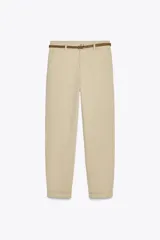 Pantalón chino color beige, de tiro medio, con bolsillos frontales y traseros. Incluye cinturón trenzado marrón.