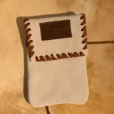 Funda para celular de gamuza azul marino con correa de cuero marrón y aplique de cuero marrón con logo de la marca.