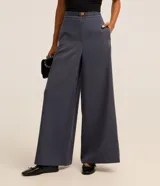 Pantalón pantalona de sastrería color gris azulado, de corte amplio y sin estampa. Tiene elástico en la espalda, cinturón en el mismo tejido y hebilla metalizada.