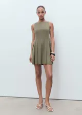 Vestido corto color verde militar, sin mangas, con cuello barco y falda evasé con pliegues.