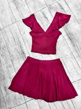 Conjunto color vino compuesto por un top con escote en V, breteles finos, volados en los hombros y elástico en la cintura, y un short pollera con cintura alta y corte acampanado.