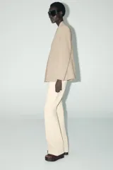 Blazer color beige, sin solapa, de manga larga con bolsillos de vivo en el delantero y cierre frontal con gancho metálico.