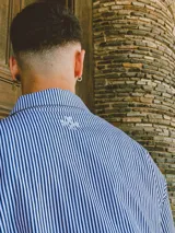 Camisa de manga corta con corte híbrido boxy fit/oversize, confeccionada en algodón. Disponible en tres diseños: a cuadros marrones, a rayas blancas y negras, y a rayas burdeos y blancas. Presenta bordados de diseño propio de la marca.