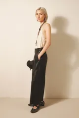 Pantalón ancho de cuero ovino color negro, con pinzas delanteras, cierre con snaps metálicos y tiras ajustables en la cintura.