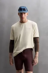 Camiseta color crema de corte holgado, cuello redondo y manga corta. Presenta un pequeño estampado con texto en el lado izquierdo del pecho.