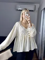 Blusa color crema con escote en V, mangas largas abullonadas con puños elásticos y detalles de encaje y bordado en el frente.