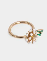 Anillo dorado con dije de flor con pétalos blancos y centro amarillo, y una hoja verde esmaltada.