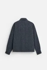 Camisa de hombre a cuadros azules y negros, de corte cuadrado, con cuello solapa, manga larga con puños abotonados, cierre frontal con botones y bolsillos de parche con solapa en el pecho.