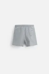Short de baño con textura seersucker a rayas verticales azul marino y blanco. Tiene cintura elástica ajustable con cordón, bolsillos frontales y traseros, aberturas laterales en el bajo y forro interior.