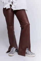 Pantalón de cuero marrón chocolate, de tiro alto, corte recto con leve flare y aberturas en el ruedo. Presenta costuras marcadas y trenzado lateral.