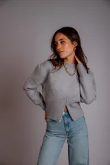 Buzo gris de punto con cuello redondo, mangas largas abullonadas y cierre frontal asimétrico.