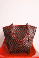 Bolso tote de cuero trenzado en tonos marrón y negro, con asas de cuero trenzado color bordó.