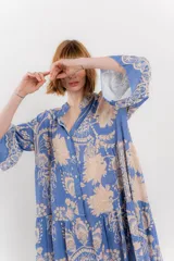 Vestido largo azul con estampado floral en tonos beige, confeccionado en viscosa. Presenta escote en V, botonadura completa en el frente y mangas largas con volados.