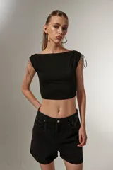 Top corto negro sin mangas, con cuello bote, frunces y cordones en los hombros. Corte ajustado al cuerpo.