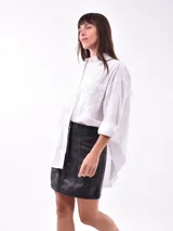 Camisa negra de corte recto, con cuello clásico, cierre frontal con botones y mangas largas con puños abotonados. Presenta dos bolsillos de parche en el pecho con apliques de tachas blancas formando un patrón geométrico.