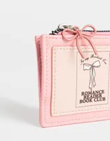 Monedero de cuerina color crudo con cierre superior, bolsillo frontal estampado con motivos japoneses y dije colgante de pagoda roja.