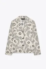 Blazer de tejido con estructura color crudo, con estampado de flores bordadas en negro. Tiene cuello solapa, manga larga y cierre frontal con botones negros.