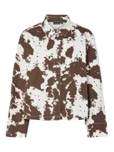 Chaqueta de jean con estampado animal print de vaca en tonos marrones y blancos, corte recto, cuello camisero y cierre frontal con botones.