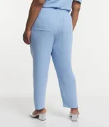Pantalón de crepé celeste, modelo zanahoria, con elástico y lazo en la cintura. Presenta bolsillos traseros simples y bolsillos delanteros con solapas y botones metalizados.