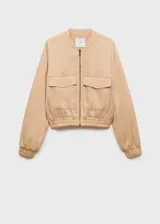Chaqueta bomber color beige con cierre frontal, cuello redondo, mangas largas con puños elásticos y dos bolsillos delanteros con solapa.
