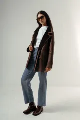 Gamulán de color marrón con interior de corderito al tono, cuello de solapa ancha, cierre frontal con botones y bolsillos laterales con solapa.