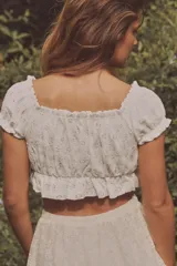Top crop blanco de escote cuadrado y manga corta abullonada. Detalle de lazada en el pecho y volantes en el escote y el bajo.