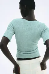 Top color celeste con textura arrugada, escote en V, mangas cortas y frunces en el delantero y los laterales.