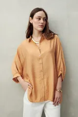 Camisa celeste de calce relajado con cuello clásico, mangas tres cuartos amplias y botones nacarados.