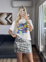 Remera blanca de cuello redondo y manga corta con estampado de frutas sobre un mantel a cuadros azules.