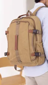 Mochila de tela canvas color beige con detalles en símil cuero marrón. Tiene presillas y broches plásticos para ajustar, bolsillo frontal con cierre, repartición interna para laptop, bolsillos laterales, correas cortas para usar como bolso de mano y correas regulables para la espalda.