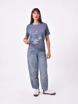 Remera blanca de algodón con cuello redondo y manga corta. Presenta un pequeño bordado en el pecho izquierdo con una figura que parece ser una persona acostada en una tabla de surf o flotador.