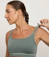 Top deportivo negro, corte tipo bralette, con escote asimétrico y doble tirante en los hombros. Presenta una banda elástica inferior con una delgada línea blanca horizontal.