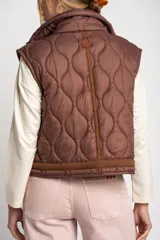 Chaleco marrón acolchado con cuello alto, cierre frontal con broches a presión y dos bolsillos delanteros con cordón ajustable.