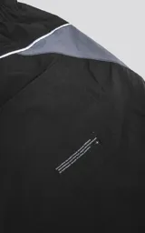 Bermuda negra de calce oversize confeccionada en textil liviano, con elástico en la cintura, cordón de ajuste, bolsillos delanteros y traseros, y detalles de recortes en gris y blanco.