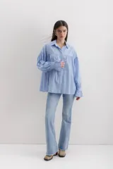 Camisa gris a rayas verticales blancas, de corte amplio, cuello alto con lazo y mangas largas abullonadas con puños elásticos.